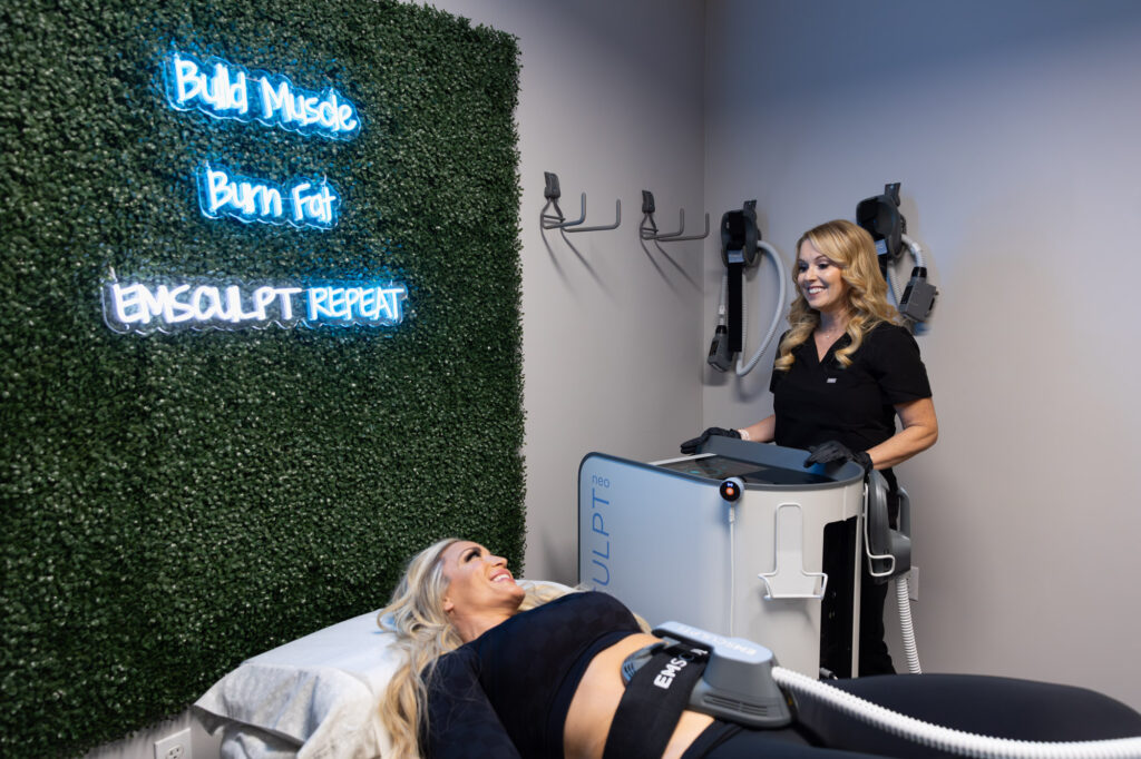 A provider smiles at a patient laying on her back before starting a session for Emsculpt NEO in St. Petersburg